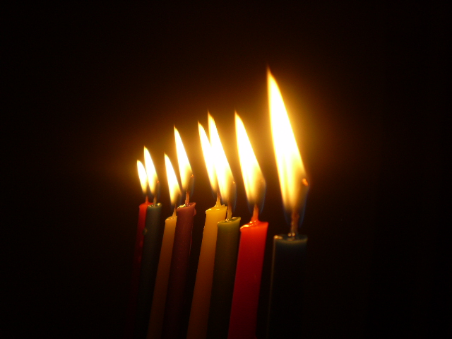 Eight colorful Hanukkah candles, lit, against a dark background