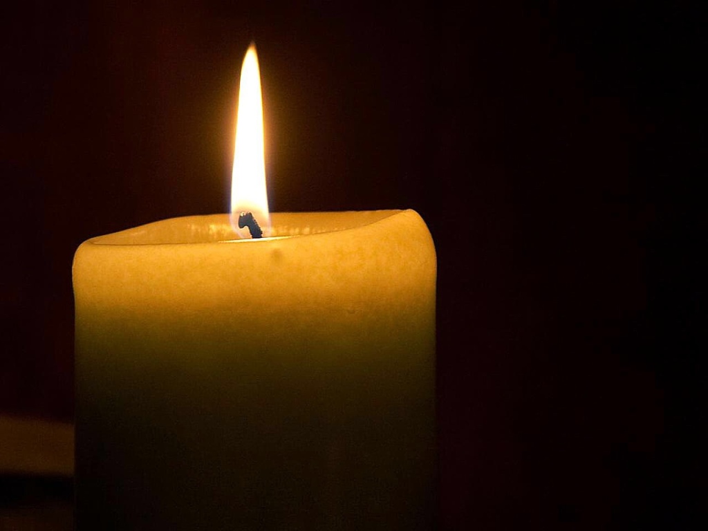 A Shabbat candle burning against a black backdrop.